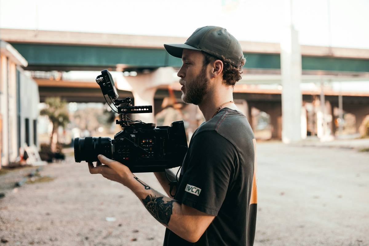 Smiling filmmaker holding an umbrella while filming near puddles